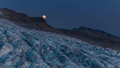 पहाड़ों के साथ एक ग्लेशियर पर चंद्रमा बढ़ रहा है